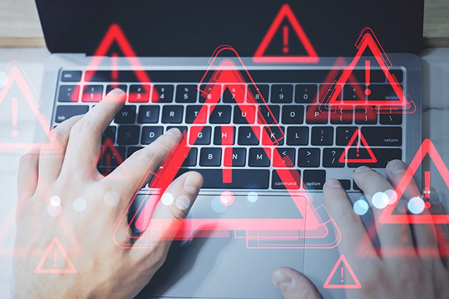 a hand typing on a laptop with red alert marks